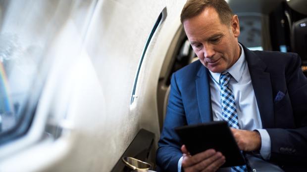 A man in a suit sits by the window of a private plane