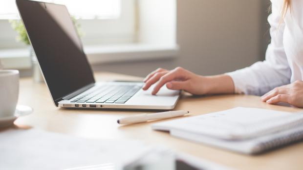 A businesswoman in a white shirt sits at a desk using a laptop